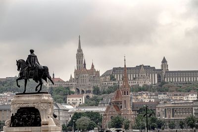 Statue in city against cloudy sky