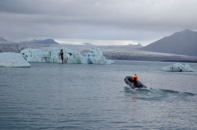 Man on inflatable motorboat on frozen sea against sky