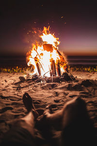 Unrecognizable crop male tourist lying on sandy seashore and enjoying warm campfire during sunset in summer