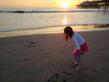 Girl walking at beach against sky during sunset