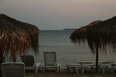 Empty chairs and tables on beach against sky