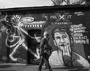 Full length of man standing against graffiti wall of building