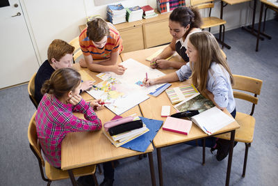 High angle view of students discussing over map in classroom