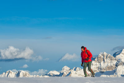 Rear view of woman walking on snow covered landscape against sky