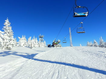 Ski lift over snow covered mountains against blue sky