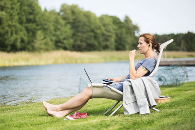 Full length side view of mature woman using hands-free device at lakeshore