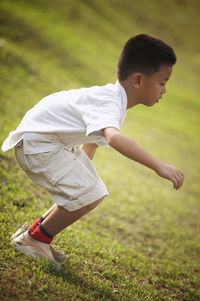 Side view of boy standing on grassy field while playing at park