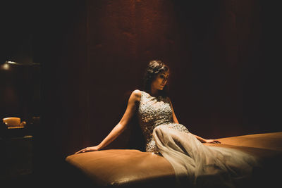 Young woman in dress sitting on bed at home