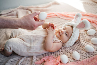 Dad plays with a newborn baby who lies on a bed in pastel colors 