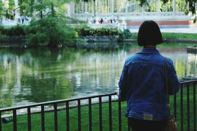 Rear view of man standing by railing against river