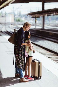 Smiling mother and daughter waiting on platform at train station