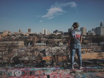 Rear view of man looking at buildings while standing on terrace in city