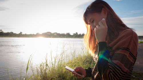 Young woman using smart phone against sky