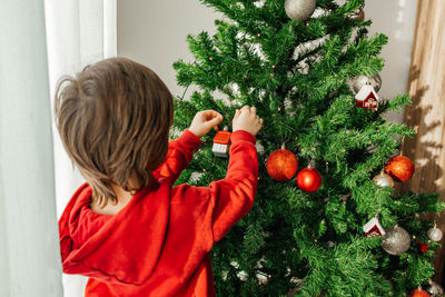 A charming little boy hangs new year's toys on the christmas tree. children celebrate new year 