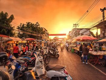 People at street market in city against sky during sunset