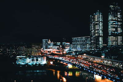 Illuminated buildings by river against sky at night