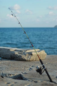 Fishing rod on rock by sea against sky