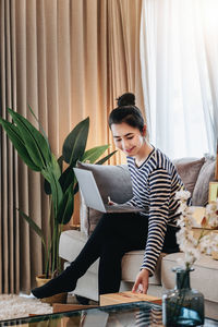 Young woman with laptop sitting on sofa at home