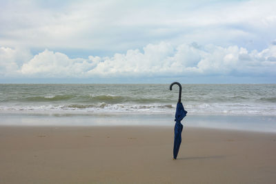 A closed umbrella is stuck in the sand on the beach in front of the ocean with waves
