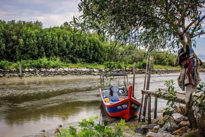 Boat moored on river by trees against sky