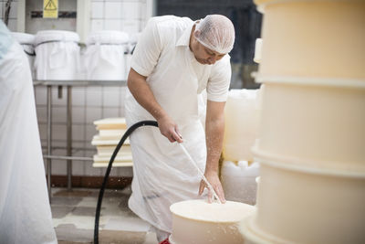 Cheese factory worker cleaning containers with hose