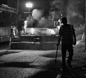 Manual worker with tool walking on roadside at construction site during night