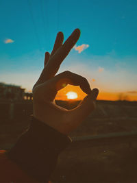 Close-up of hand holding candle against sky during sunset