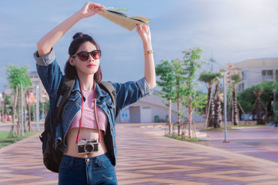 Young woman wearing sunglasses standing against sky in city