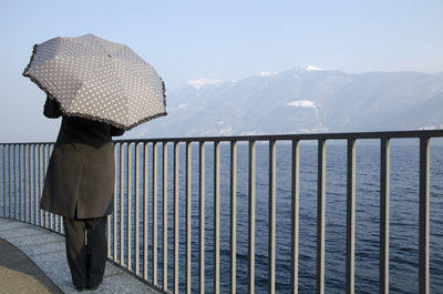 Rear view of woman standing on railing against snowcapped mountains