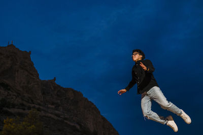 Young transgender man jumping outdoors at night.