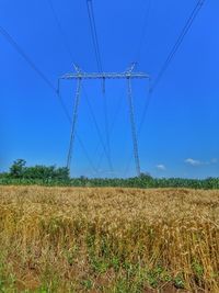 Low angle view of electricity pylon on field against blue sky