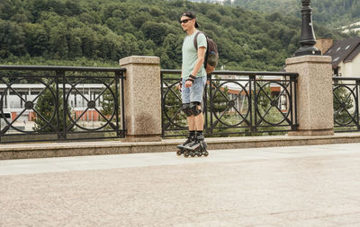 Young man in blue in protective equipment riding on roller skates along embankment 