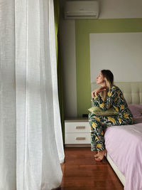 Side view of woman sitting on bed at home