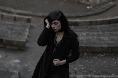 Young woman looking away while standing against wall