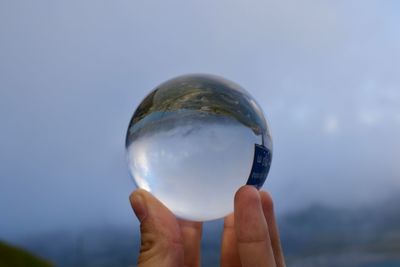 Cropped hand holding crystal ball against cloudy sky