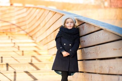 A 5-year-old girl is standing on a wooden staircase.