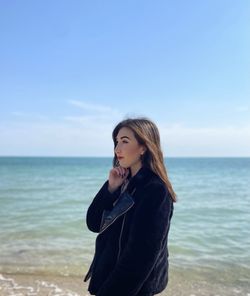 Young woman standing at beach against sky