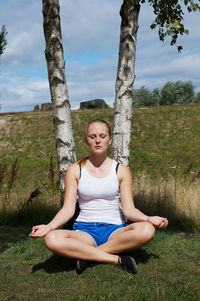 Woman practicing yoga in field during sunny day