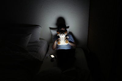 High angle view of woman lying on bed holding stuffed toy in darkroom