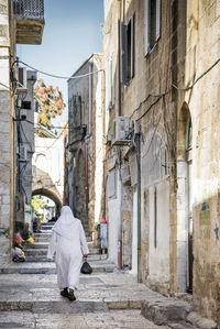 Rear view of woman walking on street amidst buildings