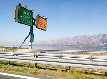 Road sign by footpath against clear blue sky