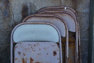 Close-up of rusty folded metal chairs against wall