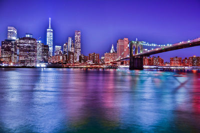 Illuminated brooklyn bridge over east river against sky at dusk