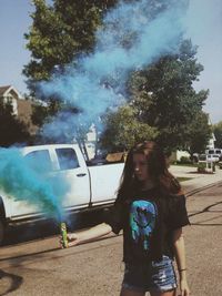 Young woman holding blue distress flare while standing outdoors