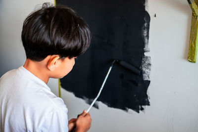 Young child painting a wall in black colour. view from behind.