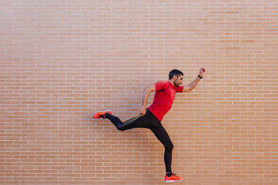 Full length of man with arms raised against brick wall