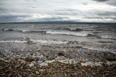 View of calm beach against cloudy sky