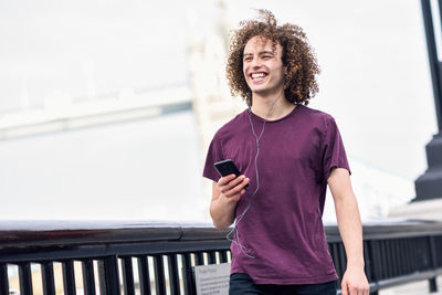 Smiling young man using mobile phone while standing by railing