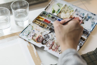 Cropped image of artist mixing watercolor paints while working in creative office