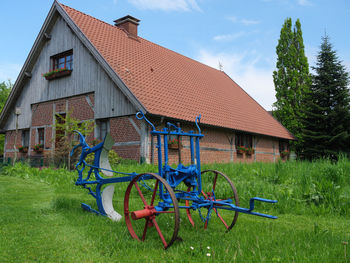 Bicycle by house on field against sky